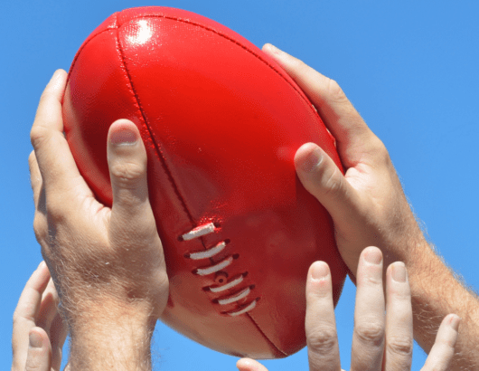 Two sets of hands reaching for a red football